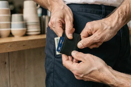 Homme sortant un porte-cartes slim noir de sa poche de pantalon dans un café contemporain